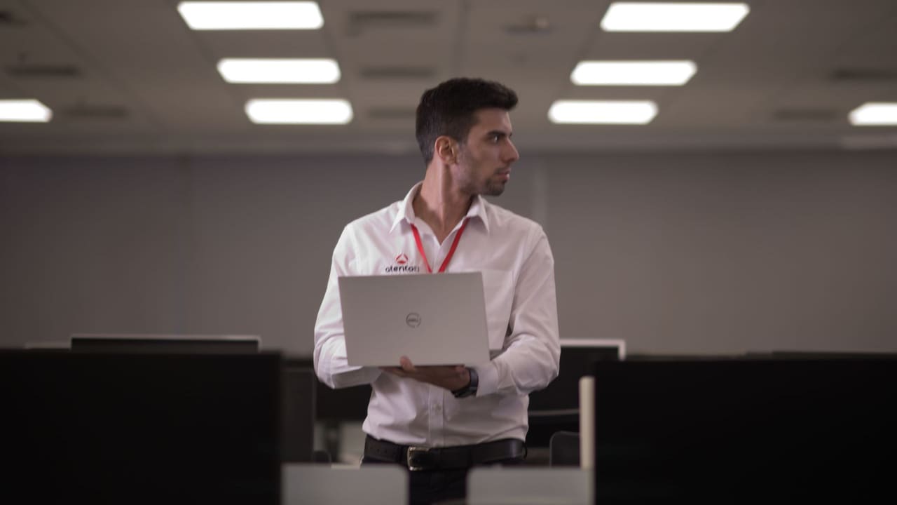 Técnico da AtentoTI com crachá, circulando com o notebook entre as mesas do escritório do cliente.